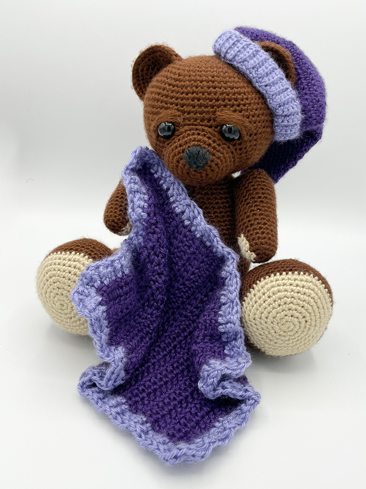 Brown teddy bear with purple night cap and blanket
